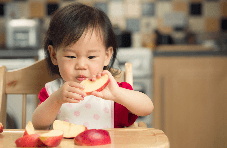 A baby sat in a high chair eating an Apple Snack